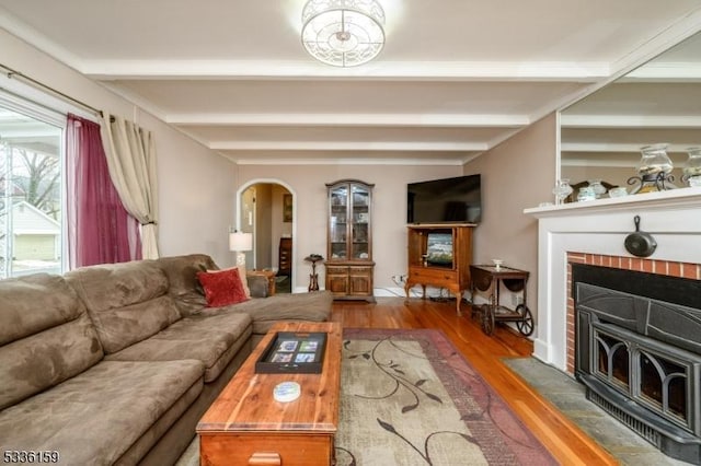 living room featuring beam ceiling, a brick fireplace, wood finished floors, and arched walkways