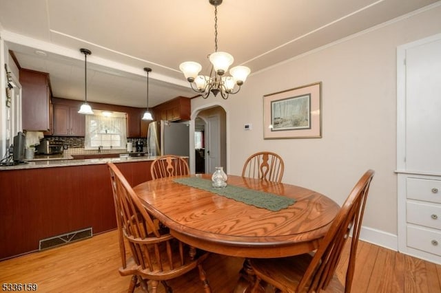 dining area featuring light wood finished floors, visible vents, ornamental molding, arched walkways, and a notable chandelier