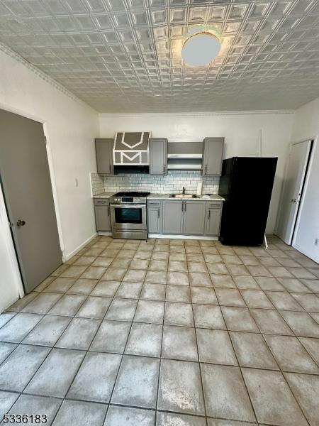 kitchen featuring stainless steel range with gas stovetop, light countertops, gray cabinets, freestanding refrigerator, and an ornate ceiling