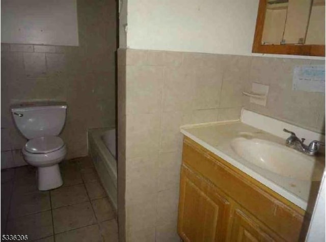 bathroom with tile walls, vanity, tile patterned floors, a tub, and toilet