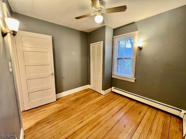 unfurnished bedroom featuring a baseboard radiator, ceiling fan, light wood-type flooring, and a closet