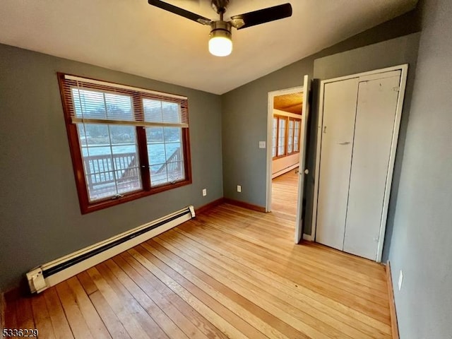 unfurnished bedroom with vaulted ceiling, ceiling fan, baseboard heating, and light hardwood / wood-style floors