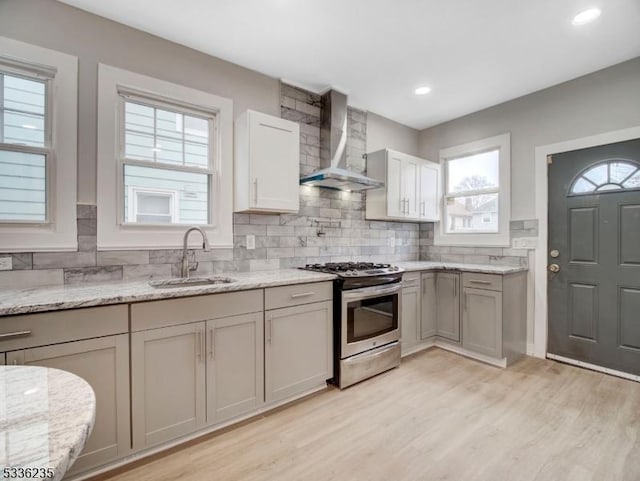 kitchen featuring sink, backsplash, light hardwood / wood-style floors, gas stove, and wall chimney range hood