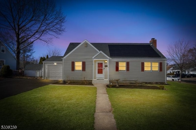 view of front facade featuring aphalt driveway, a yard, an attached garage, solar panels, and a chimney