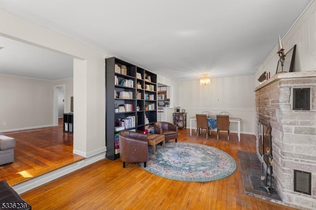 living area featuring visible vents, wood finished floors, an inviting chandelier, baseboards, and a brick fireplace