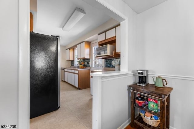 kitchen with backsplash, light countertops, freestanding refrigerator, and a sink