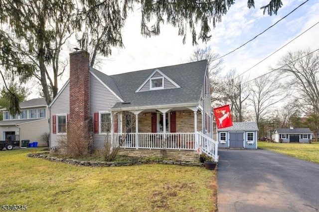 cape cod home featuring a front lawn, covered porch, and a storage shed