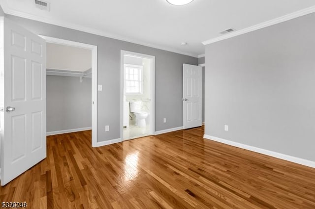 unfurnished bedroom featuring ensuite bathroom, hardwood / wood-style floors, a walk in closet, crown molding, and a closet