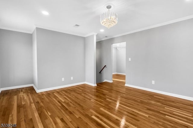 empty room featuring hardwood / wood-style flooring, crown molding, and a chandelier