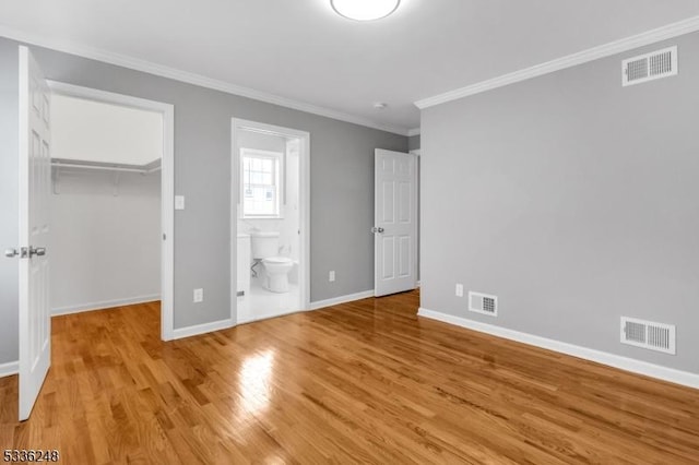 unfurnished bedroom featuring ensuite bathroom, a spacious closet, light wood-type flooring, ornamental molding, and a closet