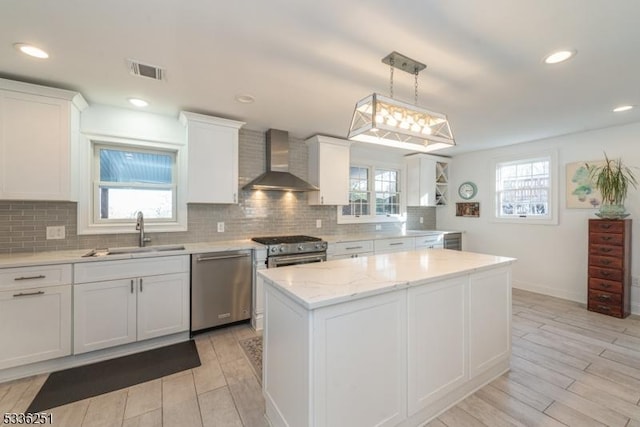 kitchen with wall chimney range hood, stainless steel appliances, a center island, white cabinets, and decorative light fixtures