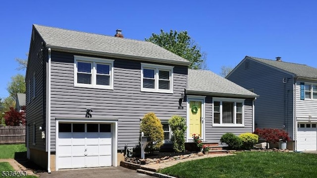 split level home with fence, a shingled roof, a front lawn, a garage, and a chimney
