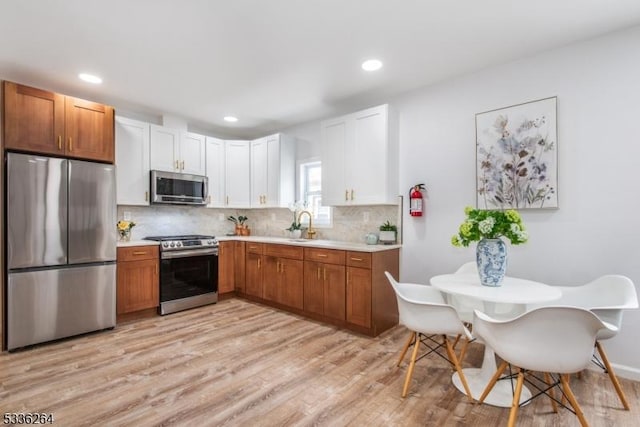 kitchen with appliances with stainless steel finishes, white cabinetry, sink, backsplash, and light hardwood / wood-style floors