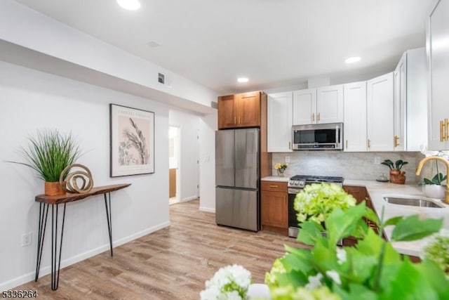 kitchen with sink, light hardwood / wood-style flooring, appliances with stainless steel finishes, white cabinetry, and tasteful backsplash