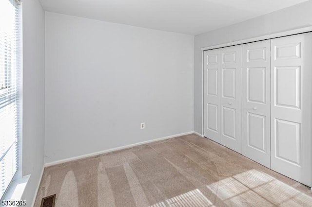 unfurnished bedroom featuring multiple windows, light colored carpet, and a closet