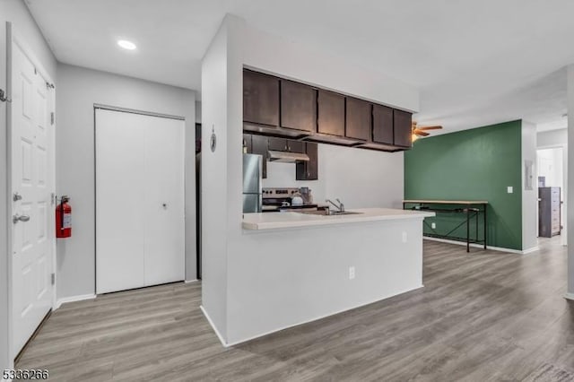 kitchen featuring dark brown cabinets, light wood-type flooring, kitchen peninsula, ceiling fan, and stainless steel appliances