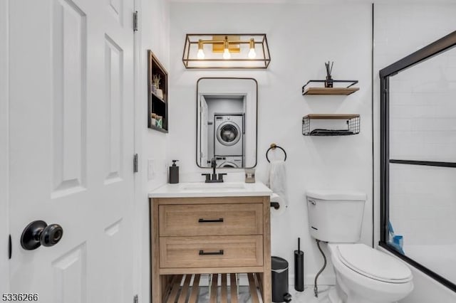 bathroom featuring vanity, stacked washer / drying machine, a shower with shower door, and toilet