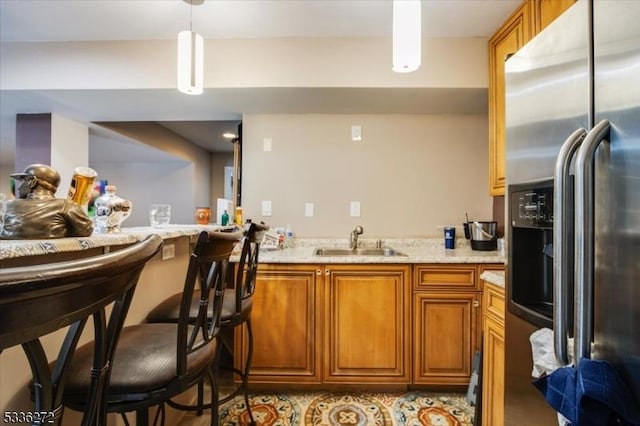 kitchen with decorative light fixtures, sink, a kitchen breakfast bar, stainless steel fridge with ice dispenser, and light stone countertops