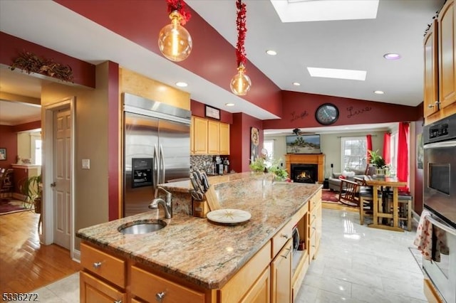 kitchen featuring stainless steel built in refrigerator, lofted ceiling with skylight, sink, light stone counters, and a center island