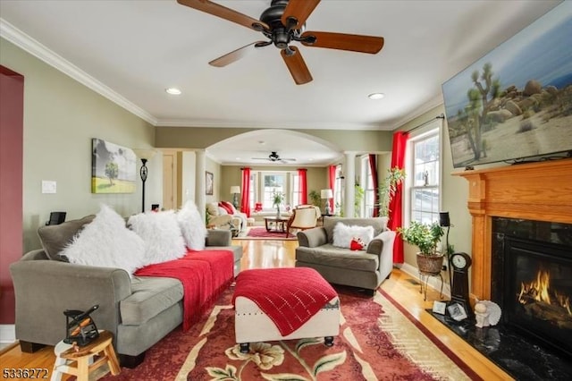 living room featuring ornate columns, crown molding, ceiling fan, a fireplace, and hardwood / wood-style floors