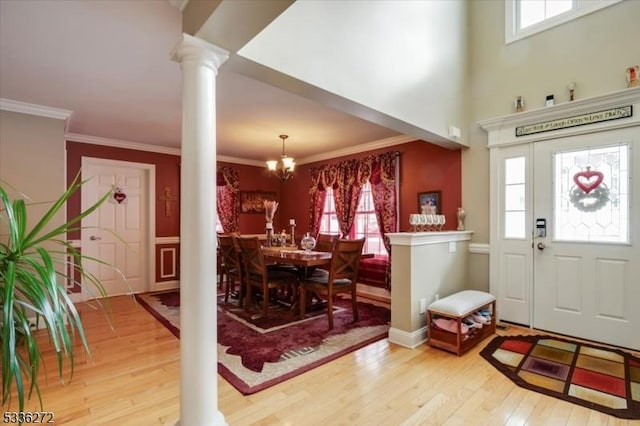 entrance foyer featuring ornate columns, crown molding, a chandelier, and light hardwood / wood-style floors