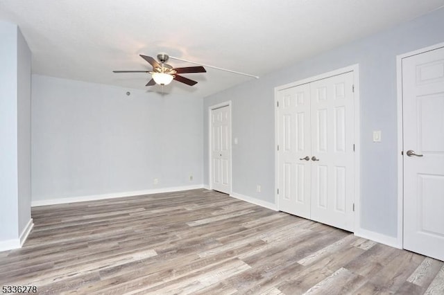 unfurnished bedroom featuring ceiling fan, light hardwood / wood-style flooring, and two closets