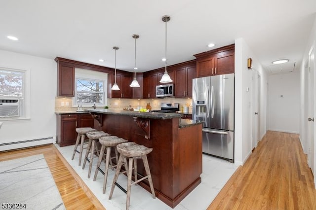 kitchen with appliances with stainless steel finishes, a kitchen island, a kitchen bar, decorative light fixtures, and a baseboard radiator