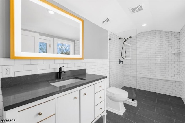 full bathroom with visible vents, toilet, vaulted ceiling, a tile shower, and tile walls