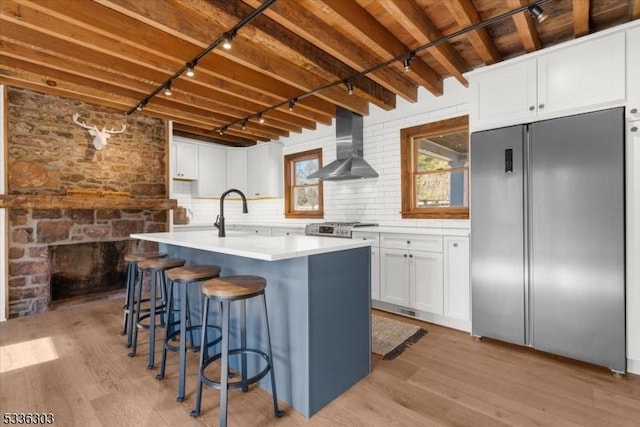 kitchen with light wood-style flooring, built in fridge, white cabinets, wall chimney range hood, and range