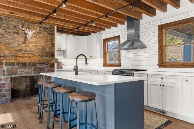 kitchen with range, wood finished floors, white cabinets, and wall chimney range hood