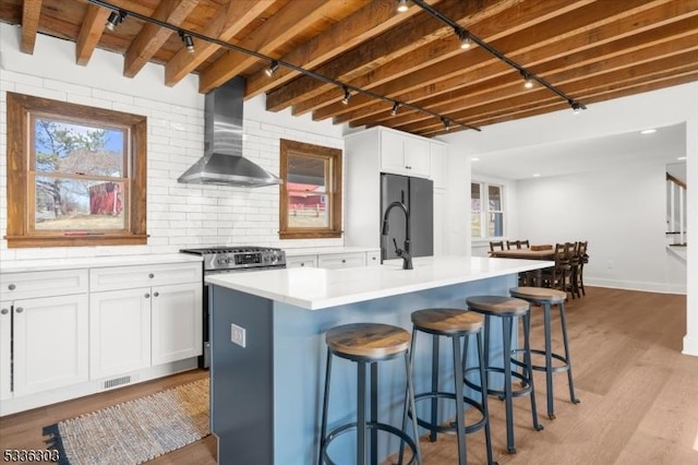 kitchen with freestanding refrigerator, white cabinets, stainless steel range with gas cooktop, and wall chimney exhaust hood