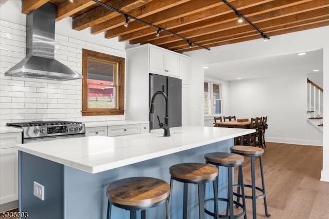 kitchen with stainless steel gas stove, wood finished floors, freestanding refrigerator, wall chimney range hood, and decorative backsplash