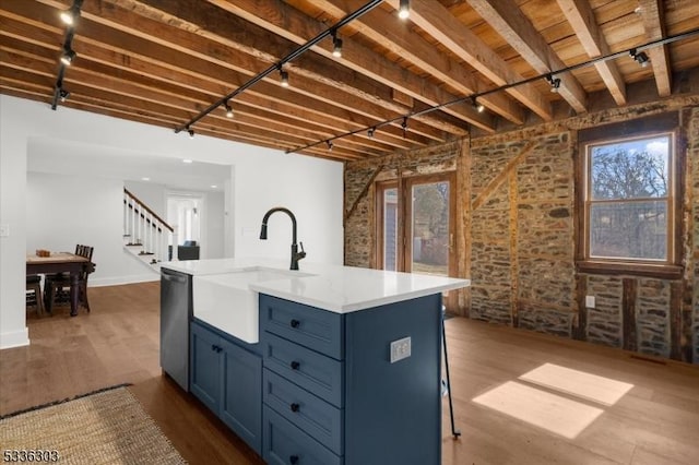 kitchen featuring brick wall, dark wood finished floors, blue cabinetry, rail lighting, and stainless steel dishwasher