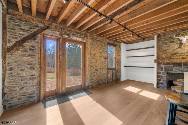 unfurnished living room featuring a stone fireplace, wood finished floors, and track lighting