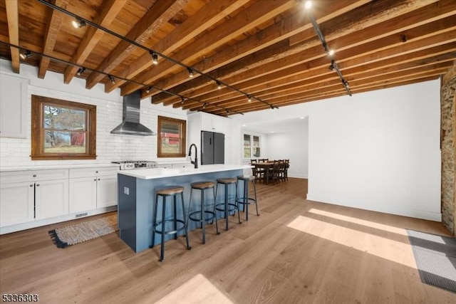 kitchen featuring light wood finished floors, wall chimney range hood, a breakfast bar area, freestanding refrigerator, and white cabinetry