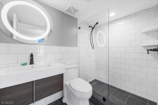 full bath featuring visible vents, toilet, vanity, tiled shower, and tile walls