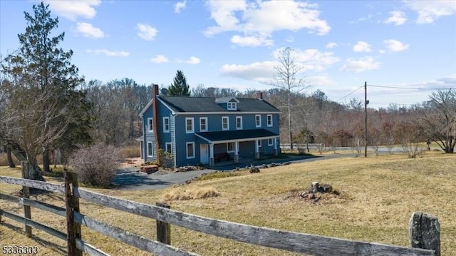 view of front of house with a front yard, fence, a forest view, driveway, and a porch