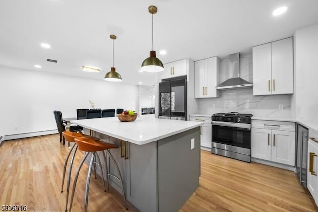 kitchen with stainless steel gas range oven, fridge, wall chimney range hood, and white cabinets