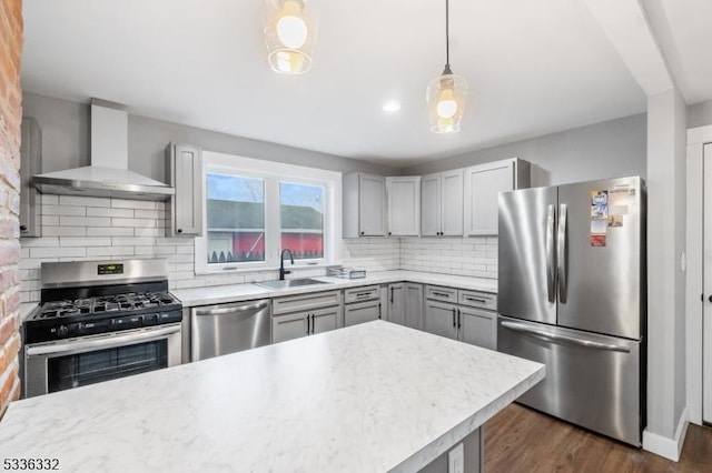 kitchen with sink, tasteful backsplash, hanging light fixtures, appliances with stainless steel finishes, and wall chimney range hood