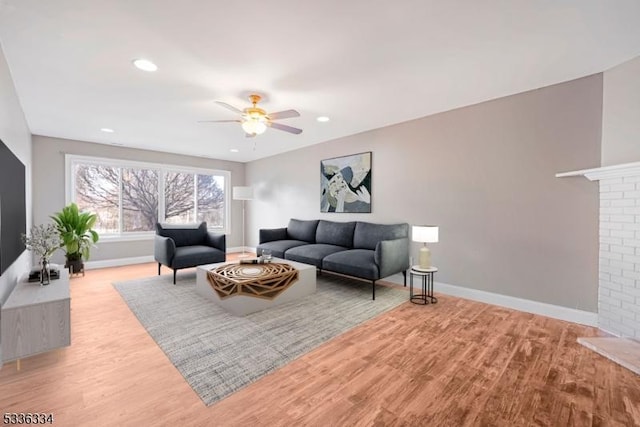 living room featuring ceiling fan, a brick fireplace, and light wood-type flooring