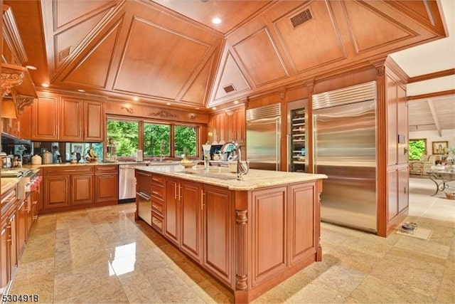 kitchen with wooden walls, stainless steel appliances, light stone counters, coffered ceiling, and an island with sink