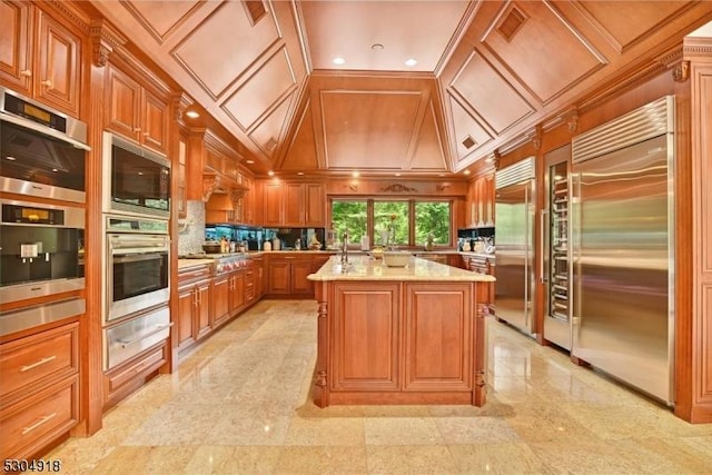 kitchen featuring lofted ceiling, sink, built in appliances, a center island with sink, and light stone countertops