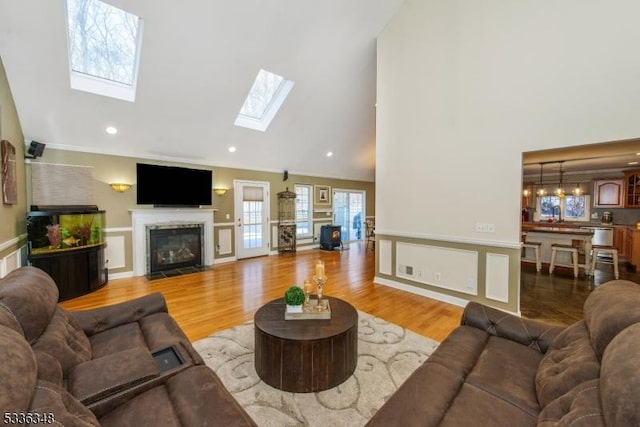 living room with crown molding, wood-type flooring, a skylight, and high vaulted ceiling