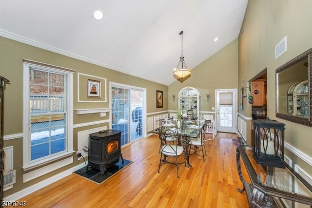 dining space with high vaulted ceiling, a wood stove, and light wood-type flooring