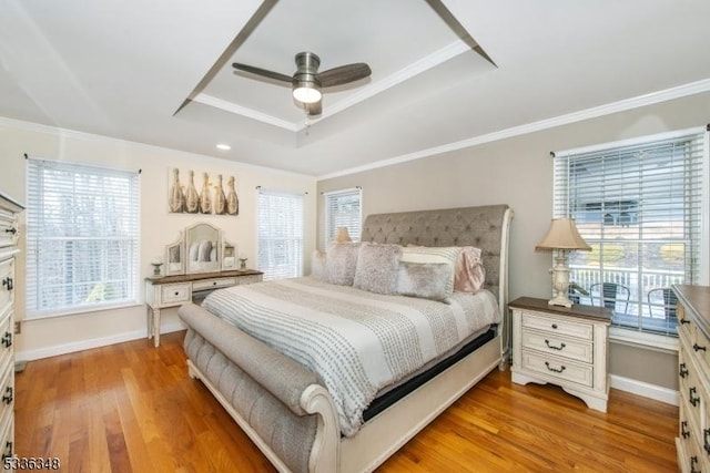 bedroom with multiple windows, a raised ceiling, and light wood-type flooring