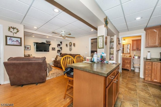 kitchen with a kitchen bar, a paneled ceiling, ceiling fan, and a kitchen island