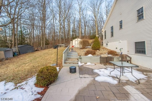 yard covered in snow featuring a patio and a storage unit