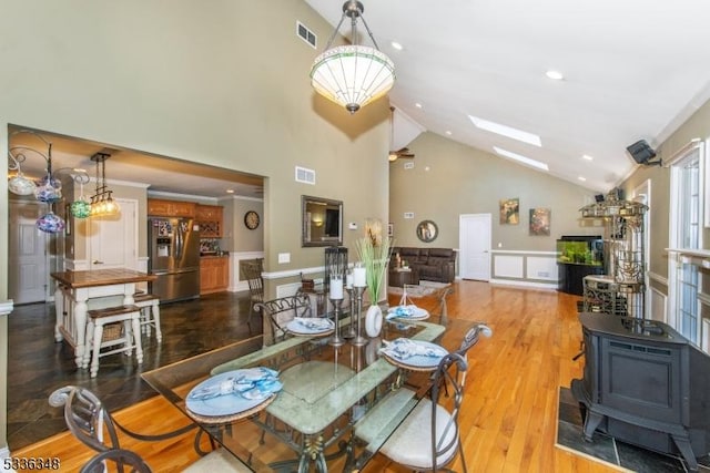 dining space featuring hardwood / wood-style flooring, a skylight, high vaulted ceiling, and a wood stove