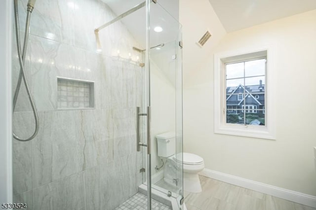 bathroom featuring a shower with door and toilet