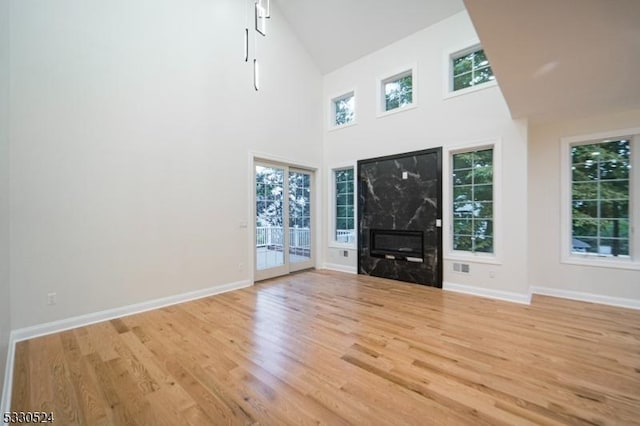 unfurnished living room featuring a premium fireplace, plenty of natural light, high vaulted ceiling, and light hardwood / wood-style floors